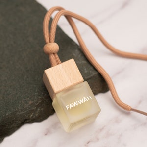 May include: A small, clear glass bottle with a wooden cap and a brown cord. The bottle is labelled "FAWWÄH".