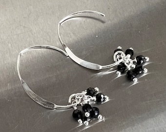 Puede incluir: Un par de pendientes de aro de plata con colgantes de piedras preciosas negras. Los pendientes son simples y elegantes, perfectos para el uso diario.