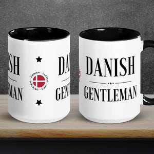 Peut inclure: Deux mugs en céramique blanche avec intérieur et anse noirs. Les mugs affichent le texte "DANISH GENTLEMAN" en gras noir. L'un des mugs présente un emblème du drapeau danois et les mots "DANISH CLASSIC MAN". Les mugs sont sur une surface en bois.