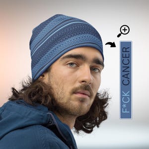 May include: A blue beanie with a tire tread pattern and light blue stripes. The beanie is worn by a person. A blue rectangle with the text "F*CK CANCER" is next to the person.