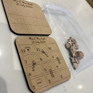 May include: A wooden game board with a snakes and ladders design. The board is brown and has a white grid with numbers 1 through 12. The board also has a start and a winner circle. The game is for Mrs. & Mrs. Scott and the date is July 21, 2024.
