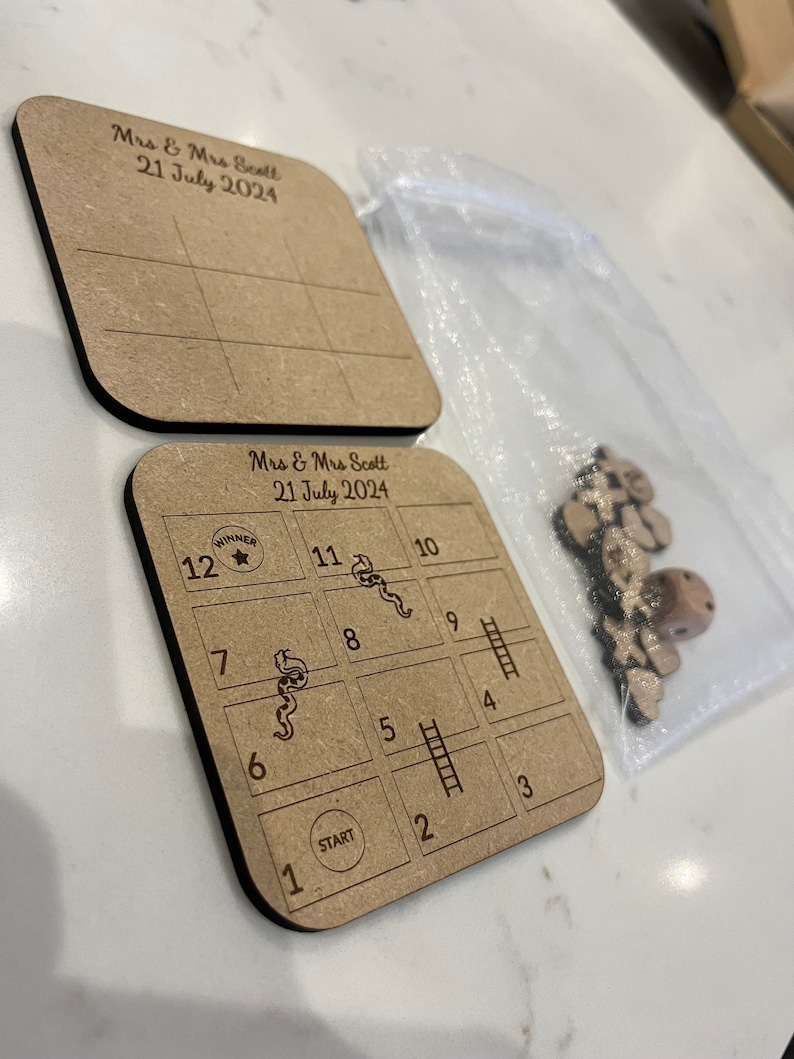 May include: A wooden game board with a snakes and ladders design. The board is brown and has a white grid with numbers 1 through 12. The board also has a start and a winner circle. The game is for Mrs. & Mrs. Scott and the date is July 21, 2024.