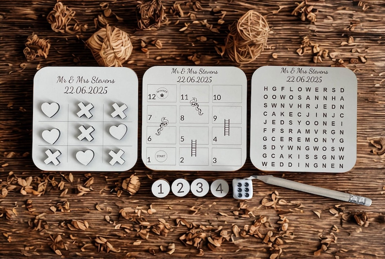 May include: A wooden wedding game set featuring tic-tac-toe, a board game, and a word search puzzle. The set includes dice, game pieces, and a pencil. The text "Mr & Mrs Stevens 22.06.2025" is printed on each game.