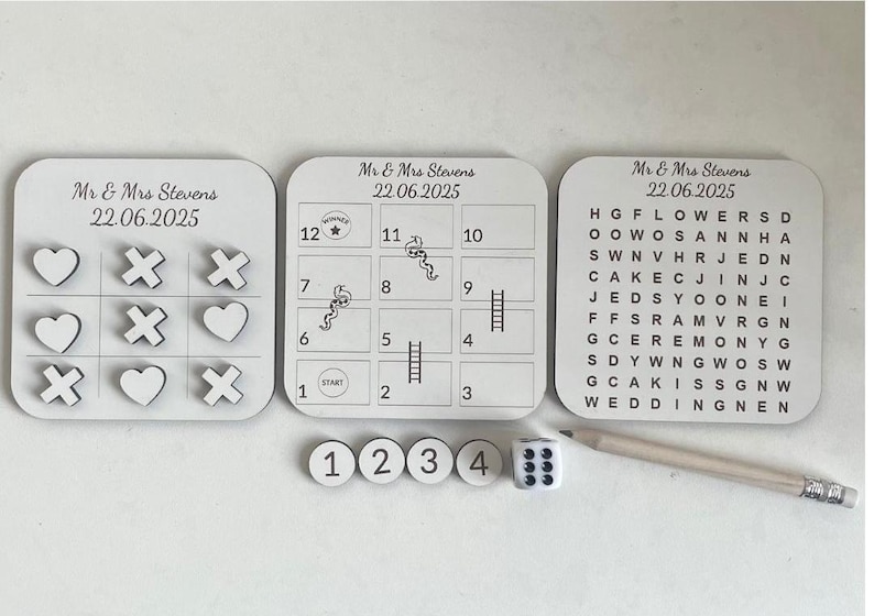 May include: A wedding game set with a tic-tac-toe board, a word search, a numbered game board, and a dice. The game boards are white with black text and graphics. The dice is white with black dots. The game set is perfect for a wedding reception or party.