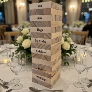 Puede incluir: Un juego de bloques de madera con las palabras "Love", "Kiss", "Hugs", "Mr & Mrs", "Yorkshire" y "Wedding" impresas en los bloques. El juego está sobre un mantel blanco con cubiertos y copas de vino.