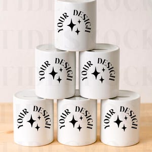 Può includere: Una pila di sette salvadanai cilindrici bianchi. Ogni salvadanaio ha una fessura e presenta la scritta "YOUR DESIGN" in un cerchio con una grafica a stella. Il design è nero.