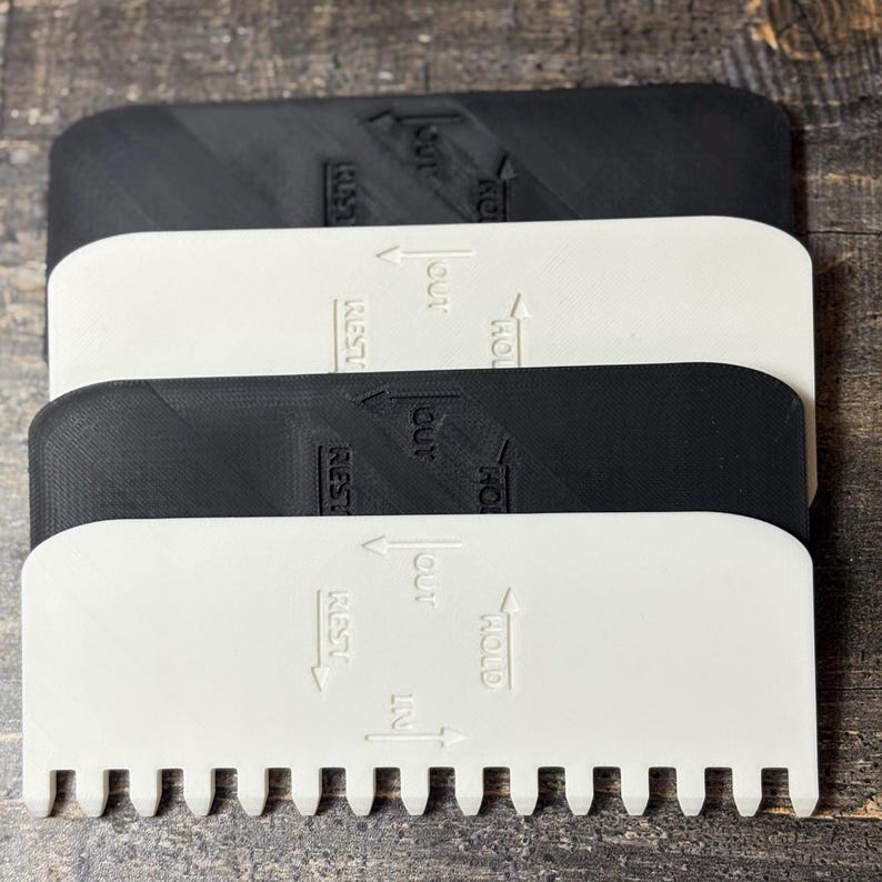 May include: A stack of four plastic tools, two black and two white. Each tool has a rectangular top with rounded corners and a row of teeth along one edge. Text and arrows indicate "IN", "OUT", "HOLD", and "REST".