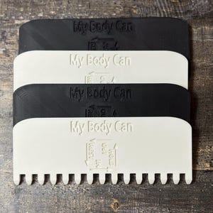 May include: Four plastic tools in black and white are stacked. Each tool has the text "My Body Can" embossed on it. The bottom edge of each tool has a series of small teeth. The text "HOLD", "REST", and "OUT" are also visible.