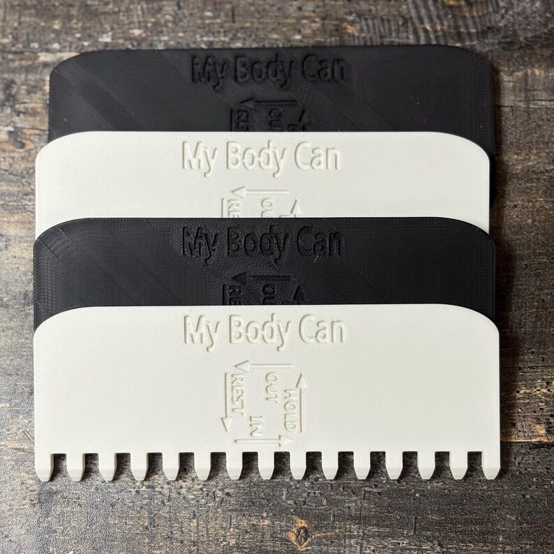 May include: Four plastic tools in black and white are stacked. Each tool has the text "My Body Can" embossed on it. The bottom edge of each tool has a series of small teeth. The text "HOLD", "REST", and "OUT" are also visible.