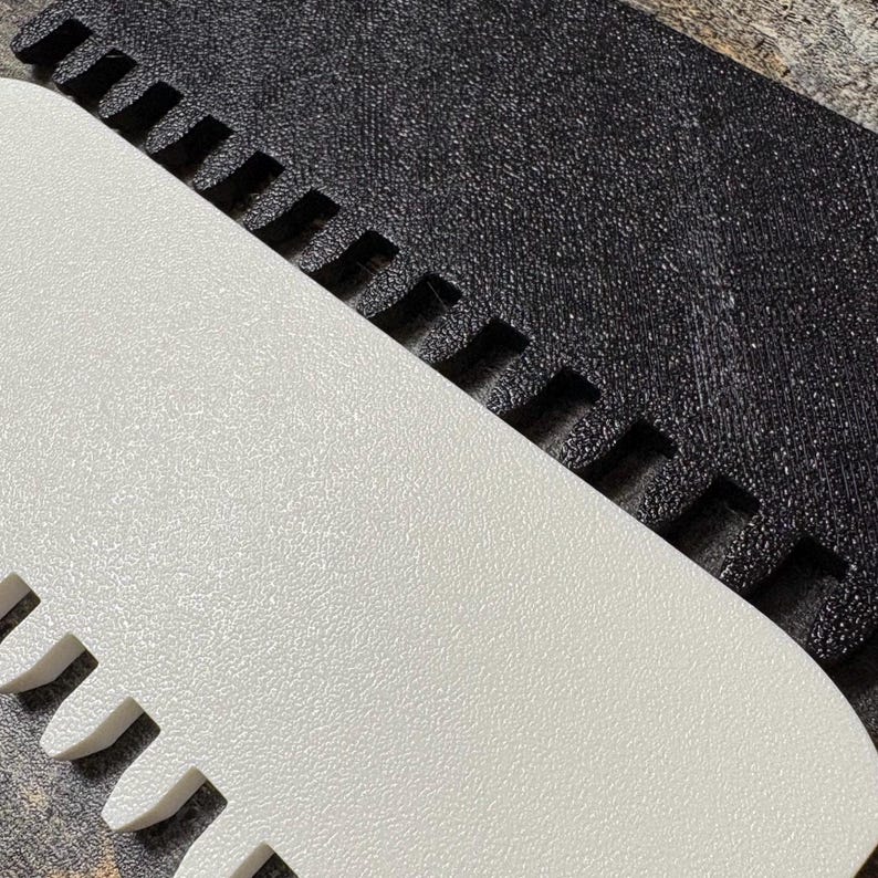 May include: Close-up of two textured, rectangular objects. One is white with a rounded edge and a series of evenly spaced, rectangular cutouts. The other is black with a similar texture and cutouts. The objects are angled towards each other.