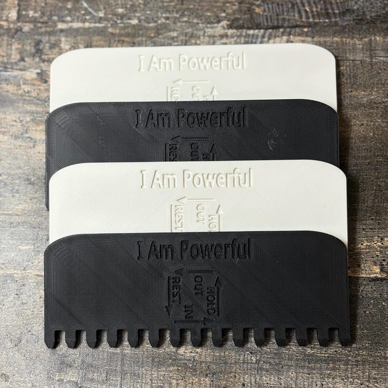May include: Four rectangular, textured tools, two white and two black, are stacked. Each tool has rounded edges and a row of teeth along one side. The text "I Am Powerful" is embossed on each tool, along with the words "Hold Out In Rest" and arrows.