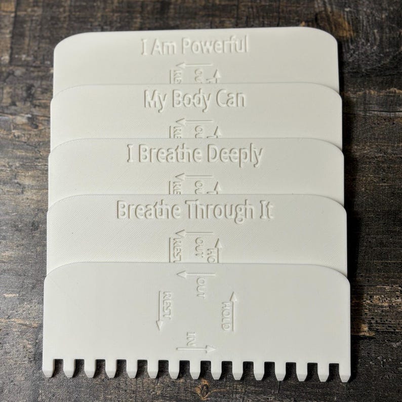 May include: A stack of white, rectangular tools with rounded edges and a notched bottom. Each tool has embossed text: "I Am Powerful," "My Body Can," "I Breathe Deeply," and "Breathe Through It." Arrows and additional text are also present.