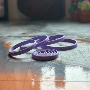 May include: A collection of purple, circular cookie cutters in various sizes. The cutters are numbered 6 through 10, with the smallest cutter in a spiral design. The cutters are made of a smooth material and are arranged on a textured surface.