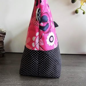 Peut inclure: Une pochette en tissu avec une section sup&eacute;rieure rose vif &agrave; motif floral noir et blanc et une section inf&eacute;rieure noire &agrave; pois blancs. Le sac comprend un anneau en D en m&eacute;tal argent&eacute; sur le c&ocirc;t&eacute; et des coutures matelass&eacute;es visibles.