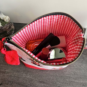 Pu&ograve; includere: Una pochette con cerniera e esterno bianco con stampa di personaggi dei cartoni animati e un fiocco rosso a pois attaccato alla zip. L'interno &egrave; foderato con un tessuto a quadretti rossi e bianchi e contiene vari articoli cosmetici.