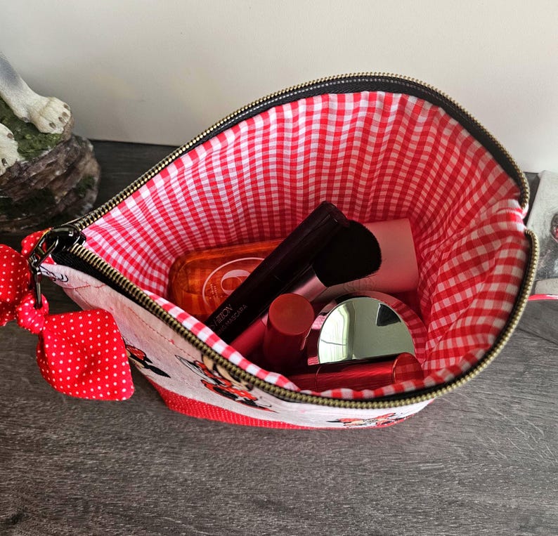 Pu&ograve; includere: Una pochette con cerniera e esterno bianco con stampa di personaggi dei cartoni animati e un fiocco rosso a pois attaccato alla zip. L'interno &egrave; foderato con un tessuto a quadretti rossi e bianchi e contiene vari articoli cosmetici.