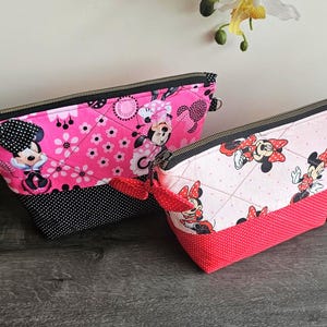 Pu&ograve; includere: Due pochette con cerniera e stampe di Minnie Mouse. La pochette pi&ugrave; grande &egrave; rosa acceso con una base a pois neri e un fiocco a pois neri. La pi&ugrave; piccola &egrave; rosa chiaro con una base a pois rossi e un fiocco a pois rossi.