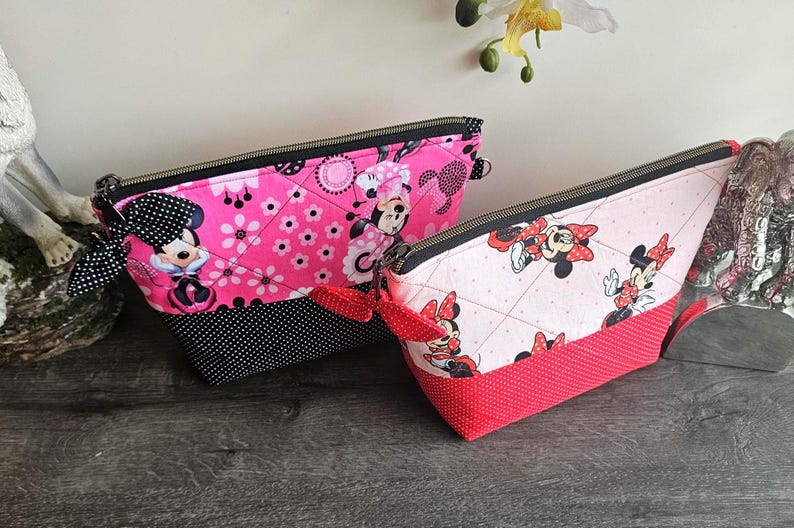 Pu&ograve; includere: Due pochette con cerniera e stampe di Minnie Mouse. La pochette pi&ugrave; grande &egrave; rosa acceso con una base a pois neri e un fiocco a pois neri. La pi&ugrave; piccola &egrave; rosa chiaro con una base a pois rossi e un fiocco a pois rossi.