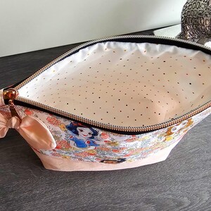 May include: A zippered pouch featuring a colorful Snow White and forest animal print on the exterior, a solid light pink base, and a light pink interior lining with small gold polka dots. The pouch includes a small pink fabric bow on the side.