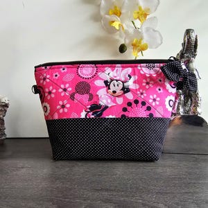 Peut inclure: Une pochette zipp&eacute;e matelass&eacute;e pr&eacute;sentant un tissu rose vif avec un motif Minnie Mouse et floral sur la moiti&eacute; sup&eacute;rieure et un tissu noir &agrave; pois blancs sur la moiti&eacute; inf&eacute;rieure. Un petit n&oelig;ud &agrave; pois noir et blanc est attach&eacute; &agrave; la fermeture.