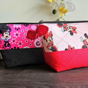 Peut inclure: Deux pochettes zipp&eacute;es matelass&eacute;es avec des motifs Minnie Mouse. La pochette de gauche est rose vif avec une base &agrave; pois noirs et un n&oelig;ud noir. Celle de droite est rose clair avec une base &agrave; pois rouges et un n&oelig;ud rouge. Fermetures noires.