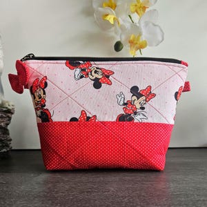 Pu&ograve; includere: Una pochette in tessuto trapuntato con un motivo ripetuto di Minnie Mouse su sfondo rosa chiaro a pois bianchi. La parte inferiore &egrave; di colore rosso tinta unita con pois bianchi. Include una chiusura a zip nera e un piccolo fiocco rosso laterale.