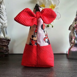 Pu&ograve; includere: Una pochette in tessuto triangolare con un motivo a pois rossi e bianchi sulla parte inferiore e una stampa di Minnie Mouse sulla parte superiore. La pochette &egrave; sormontata da un grande fiocco in tessuto a pois rossi e bianchi e una cerniera.