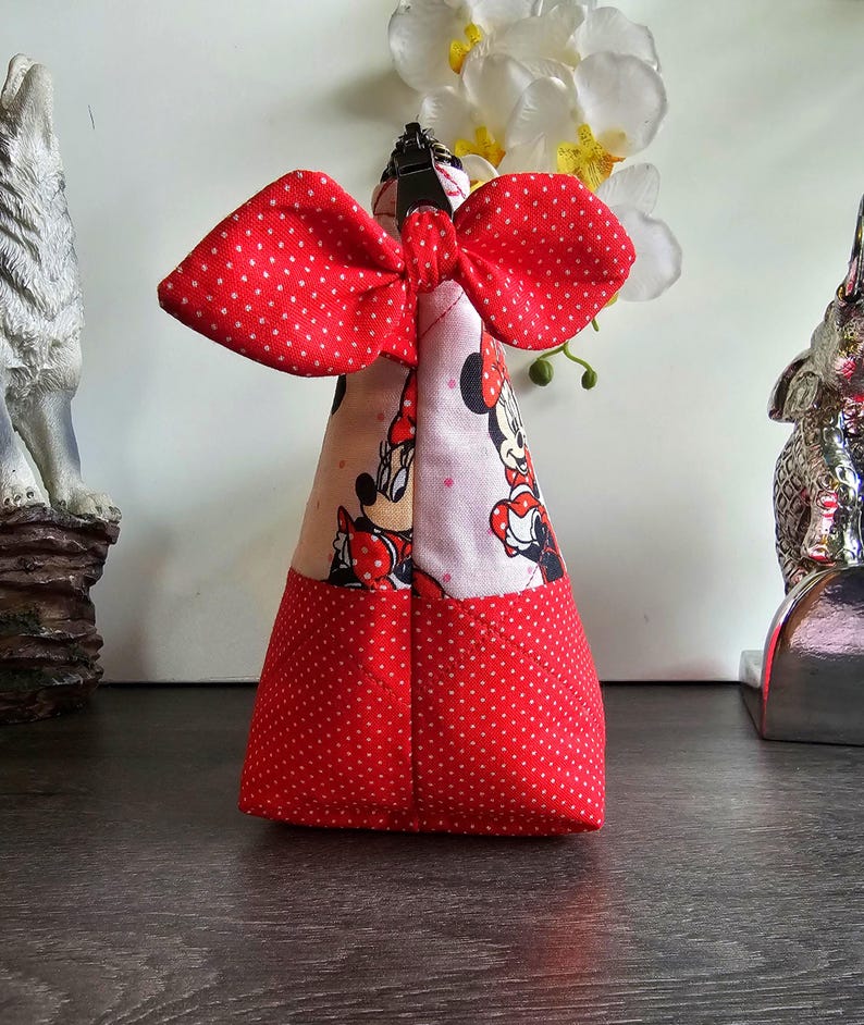Pu&ograve; includere: Una pochette in tessuto triangolare con un motivo a pois rossi e bianchi sulla parte inferiore e una stampa di Minnie Mouse sulla parte superiore. La pochette &egrave; sormontata da un grande fiocco in tessuto a pois rossi e bianchi e una cerniera.