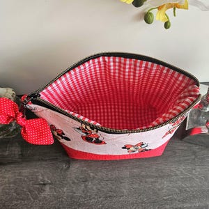 Pu&ograve; includere: Una pochette con cerniera caratterizzata da un esterno bianco con stampa di Minnie Mouse e un fiocco rosso a pois attaccato sul lato. La base &egrave; di colore rosso tinta unita e l'interno &egrave; foderato con un tessuto a quadretti vichy rossi e bianchi.