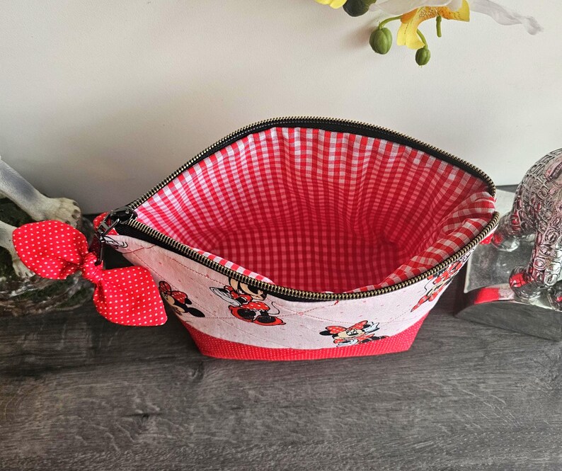 Pu&ograve; includere: Una pochette con cerniera caratterizzata da un esterno bianco con stampa di Minnie Mouse e un fiocco rosso a pois attaccato sul lato. La base &egrave; di colore rosso tinta unita e l'interno &egrave; foderato con un tessuto a quadretti vichy rossi e bianchi.