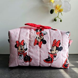 Puede incluir: Un neceser acolchado rosa con Minnie Mouse en varias poses. La bolsa tiene un lazo rojo de lunares y un cierre de cremallera. La bolsa mide aproximadamente 20 cm de largo y 13 cm de alto.