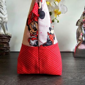 Pu&ograve; includere: Una pochette in tessuto triangolare con stampa di Minnie Mouse su sfondo chiaro e base a pois rossi e bianchi. La pochette &egrave; realizzata con cuciture trapuntate e include una piccola linguetta in tessuto rosso nell'angolo superiore per la chiusura.