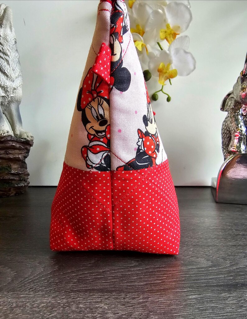 Pu&ograve; includere: Una pochette in tessuto triangolare con stampa di Minnie Mouse su sfondo chiaro e base a pois rossi e bianchi. La pochette &egrave; realizzata con cuciture trapuntate e include una piccola linguetta in tessuto rosso nell'angolo superiore per la chiusura.