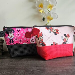 Pu&ograve; includere: Due pochette trapuntate con cerniera e stampe di Minnie Mouse. La pochette a sinistra &egrave; rosa acceso con dettagli a pois neri e un fiocco nero. Quella a destra &egrave; rosa chiaro con base a pois rossi e un fiocco rosso. Entrambe hanno cerniere nere.