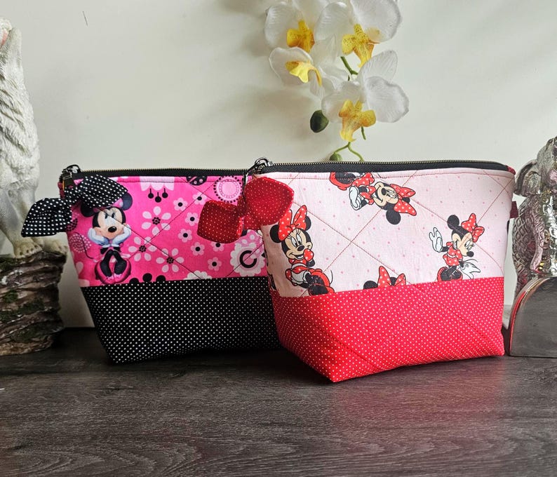 Pu&ograve; includere: Due pochette trapuntate con cerniera e stampe di Minnie Mouse. La pochette a sinistra &egrave; rosa acceso con dettagli a pois neri e un fiocco nero. Quella a destra &egrave; rosa chiaro con base a pois rossi e un fiocco rosso. Entrambe hanno cerniere nere.