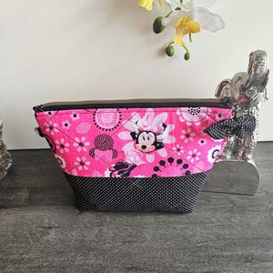 Peut inclure: Une pochette en tissu matelass&eacute; avec un fond rose vif, un imprim&eacute; Minnie Mouse, des motifs floraux blancs et des pois noirs. La partie inf&eacute;rieure est noire &agrave; pois blancs et elle est dot&eacute;e d'une fermeture &eacute;clair en m&eacute;tal.