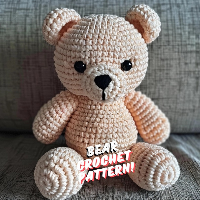 May include: A crocheted beige teddy bear with black eyes and a black nose. The bear is sitting on a gray textured surface. The text "BEAR CROCHET PATTERN!" is written in red and white letters on the bear's belly.