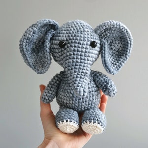 May include: A crocheted gray elephant stuffed animal with white feet. The elephant has black eyes and a textured, crocheted body.