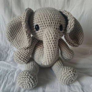 May include: A crocheted gray elephant stuffed animal with black eyes. The elephant has a long trunk and large ears.