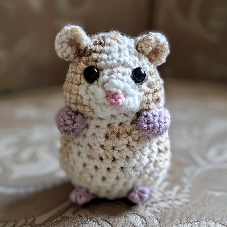 May include: A crocheted hamster toy with brown, white, and purple yarn. The hamster has black eyes and a pink nose.