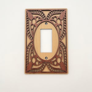 Peut inclure: Un cache-interrupteur décoratif en bois. Le couvercle présente une base marron clair avec un motif de superposition marron foncé complexe. Le motif comprend une forme ovale autour de l'ouverture de l'interrupteur et des motifs décoratifs.