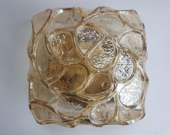 May include: A square, amber-colored glass light fixture with a textured, organic design. The fixture is composed of numerous tear-drop shaped glass pieces, creating a unique, decorative pattern. The glass has a reflective, shiny surface.