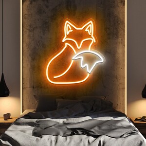 May include: A neon sign depicting an orange fox curled up with its tail wrapped around its body. The sign is illuminated with a warm white glow and is mounted on a textured wall.