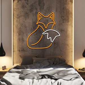 May include: A neon sign depicting a curled up orange fox with a white tail. The sign is mounted on a textured brown wall above a bed with gray bedding.