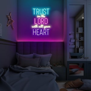 May include: A neon sign with the words "TRUST in the LORD with all your HEART" in a bedroom setting. The sign glows with blue, purple, and pink hues. A bed with gray bedding is in the foreground.