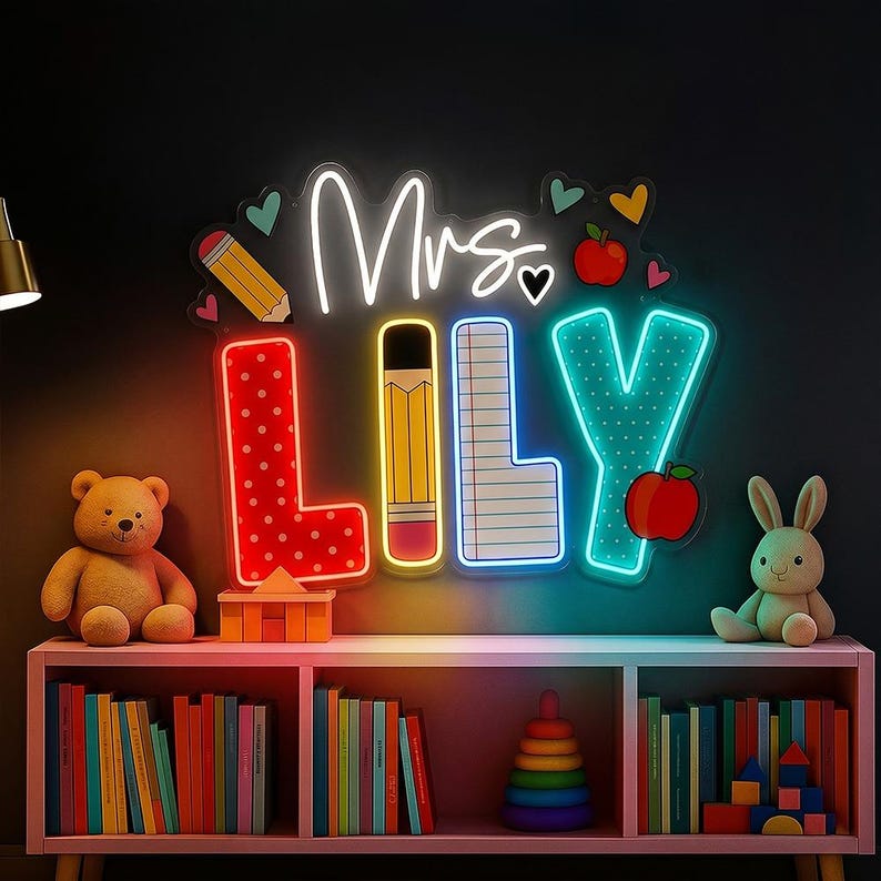 May include: A wall-mounted neon sign displaying the text Mrs. LILY in white script and block letters. The letters feature patterns of red polka dots, a yellow pencil, lined notebook paper, and teal dots, accented by small hearts and red apples.