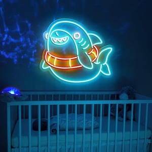 May include: A neon blue shark with a bright orange life preserver around its middle. The shark is smiling and has a white eye. The neon sign is mounted on a wall above a white crib.
