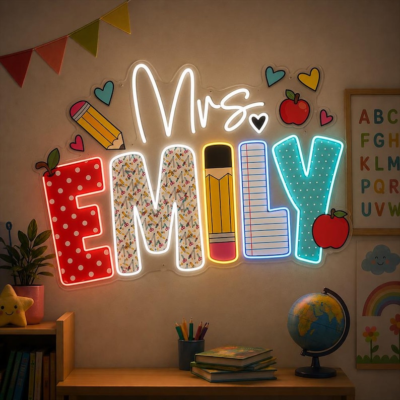 May include: A custom neon sign displaying the name Mrs. EMILY in a playful font. The letters feature school-themed patterns including red polka dots, pencils, and lined paper. The sign is decorated with neon hearts and apples.