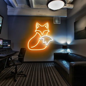 May include: A neon fox sign in orange and white, mounted on a gray wall in a room with a black leather couch and a desk with a computer monitor.