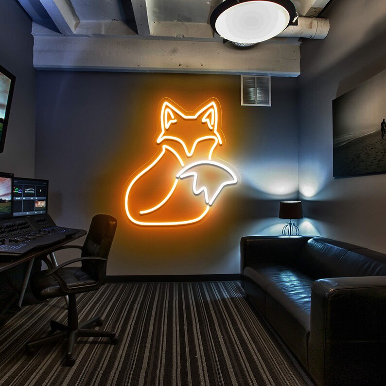May include: A neon fox sign in orange and white, mounted on a gray wall in a room with a black leather couch and a desk with a computer monitor.